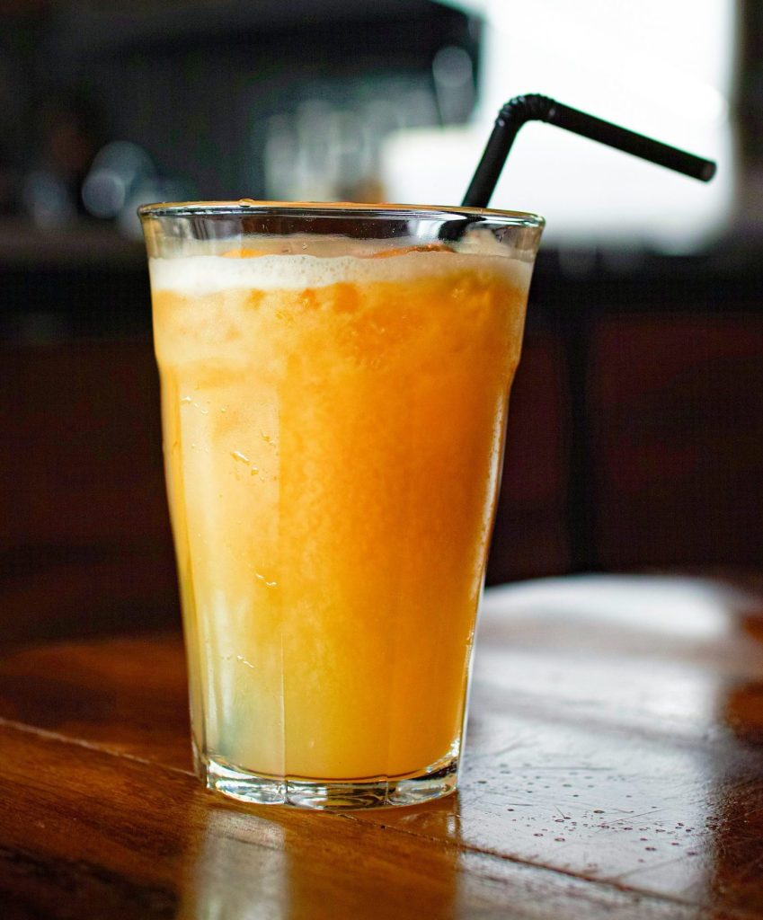 Ein hohes Glas Orangensaft mit einem Strohhalm.